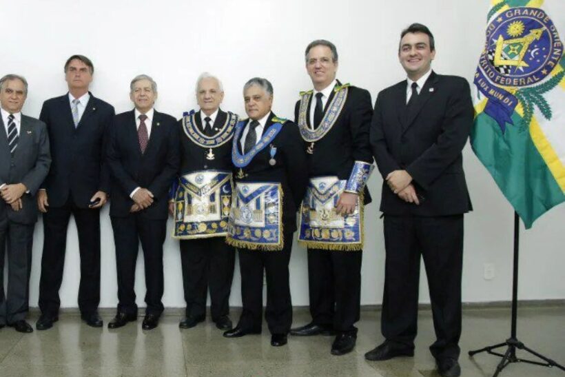 Bolsonaro ao lado de homens cm avental da maçonaria e uma bandeira da loja Grande Oriente